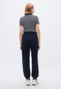 Ριγέ μπλουζάκι σε μπλε ναυτικό και λευκό συνδυασμένο με σκούρο μπλε ναυτικό παντελόνι φόρμας. Η φόρμα διαθέτει ελαστική μέση με κορδόνι και ελαστικές μανσέτες. Το outfit ολοκληρώνεται με λευκά αθλητικά παπούτσια.