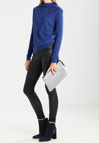 Blå stickad långärmad tröja, svarta fuskläderbyxor och marinblå ankelstövlar. Grå texturerad clutch med dragkedjedetalj avslutar outfiten.