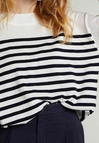 Long-sleeve top with horizontal black and white stripes, featuring a wide neckline and soft texture, paired with dark navy trousers.