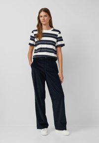 Gestreiftes Baumwoll-T-Shirt in Marineblau und Weiß, kombiniert mit weit geschnittenen Marineblauen Hosen, getragen mit weißen Sneakers. Einfaches Design mit lässiger Passform.