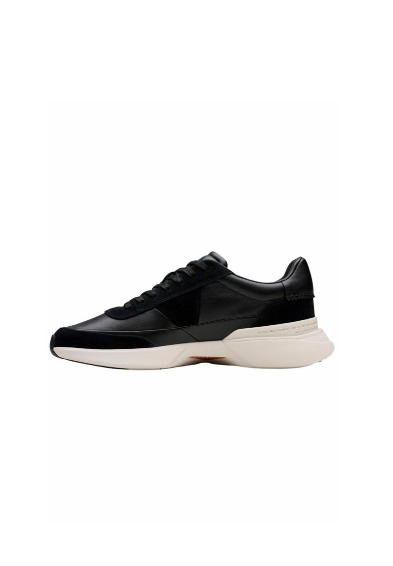 Zapatilla negra con paneles de cuero y ante, parte frontal con cordones, suela acolchada y entresuela blanca en contraste. Diseño minimalista, sin logotipos visibles.