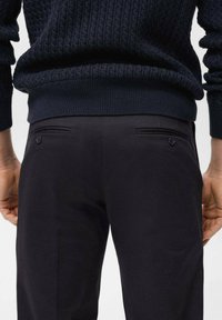 Navy ribbed knit sweater with a textured pattern and dark pants featuring back pockets and buttons. Close-up of the waist area.