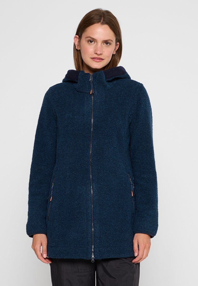Eine Frau trägt eine strukturierte, navyblaue Zip-Jacke mit Kapuze und hat zwei seitliche Reißverschlusstaschen. Sie steht vor einem schlichten, hellen Hintergrund.