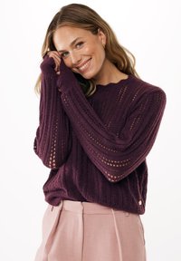 Maglione lavorato a maglia viola con una texture a costine, caratterizzato da motivi di lavorazione aperta e maniche lunghe. Abbinato a pantaloni sartoriali rosa chiaro.