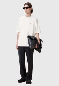 Camiseta blanca de gran tamaño con logo, pantalones holgados negros, gafas de sol negras, sosteniendo un bolso de cuero negro con correa, diseño minimalista.