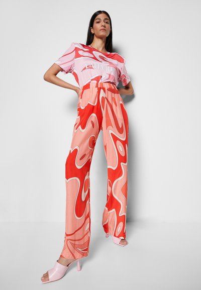 T-shirt gráfico rosa com padrões ousados em vermelho e laranja em espiral, combinado com calças largas e leves em tons vibrantes, acentuadas com saltos rosa.