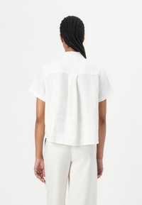 Hvit lin skjorte med kort erme og bakfold. Designet har en avslappet passform og rett nederkant, med klassisk krage.