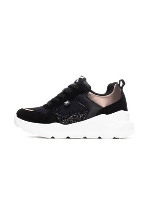 Zapatilla deportiva negra que presenta una combinación de materiales lisos y texturizados, una suela blanca y sutiles acentos metálicos en el talón.