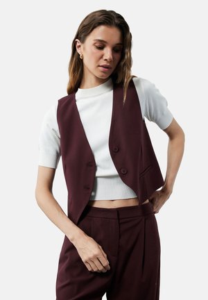Burgunderfarbener taillierter Weste mit zwei Knöpfen, kombiniert mit einem weißen Strickoberteil. Glatte Textur und strukturiertes Design mit kurzer Passform.