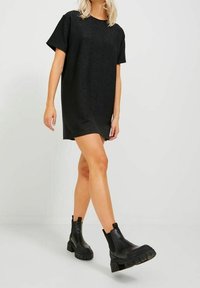 Black short-sleeve dress with a relaxed fit, made from a textured fabric. Paired with black chunky Chelsea boots.