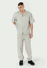 Camisa de manga curta cinza claro e calças combinando com um padrão listrado. A roupa apresenta um design com botões e um corte descontraído.