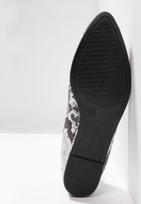Chaussure plate à imprimé serpent noir et blanc avec une semelle en caoutchouc texturée. Présente un bout arrondi et une matière supérieure lisse. Taille 37 indiquée sur la semelle.