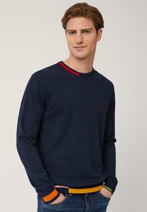 Maglione blu navy a girocollo con polsini a coste rossi e multicolori in contrasto. Tessuto liscio e design aderente, con un logo discreto.