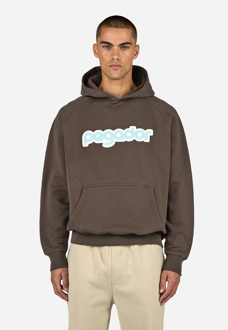 Barna kapucnis pulóver nagy világoskék „pagador” felirattal. Két első zsebe van, kötős kapucnival és bordázott mandzsettával, valamint alsó résszel.