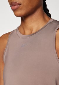 Sobiv, ilma varrukateta sporditop, mille värv on pehme beež ja tekstuur sile. Ees on väike helesinine Nike logo.