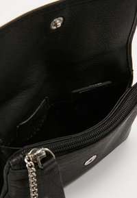 Intérieur d'un sac en cuir noir, surface texturée, fermeture à glissière et quincaillerie en métal argenté, avec une poche et doublure pour l'organisation.