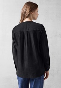 Maglietta nera a maniche lunghe con yoke posteriore, tessuto morbido, vestibilità comoda e orlo curvo. Abbinata a pantaloni in denim blu.