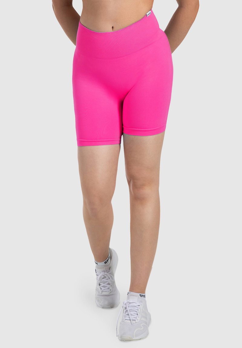 Pantalones cortos rosa de cintura alta hechos de una tela elástica, con una cinturilla acanalada y textura suave, combinados con zapatillas deportivas blancas.