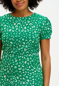 Zelené šaty s leopardím potiskem v bílé a růžové barvě, s krátkými nabíranými rukávy a kulatým výstřihem. Hladká textura látky.