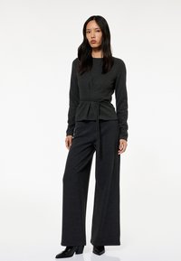 Conjunto de punto gris oscuro que incluye una blusa ajustada de estilo peplum con cintura ajustable mediante lazo y pantalones de pierna ancha, ambos hechos de una suave tela texturada.