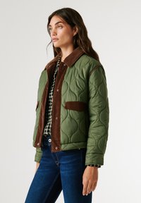 Quilted green puffer jacket with a brown corduroy collar and chest pockets, featuring a slightly oversized fit and visible stitching details.