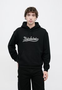 Μαύρο φούτερ με κουκούλα και μπροστινή τσέπη καγκουρό, διαθέτει τη λέξη "Dickies" σε λευκή κεντητή γραφή στο στήθος, κατασκευασμένο από απαλό ύφασμα.