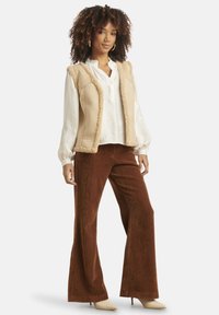 Beige fleece vest with shearling trim over a white long-sleeve blouse, paired with brown corduroy flared pants and beige pointed-toe heels.