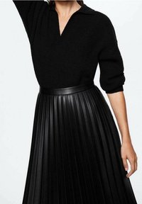 Pull en maille noir avec un col polo et des manches trois-quarts, associé à une jupe plissée en cuir synthétique noir.