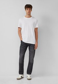 Weißes Baumwoll-T-Shirt, dunkle Jeans aus Denim und weiße Turnschuhe. Einfaches Design mit kurzen Ärmeln und einer leichten Rundung am unteren Saum des Shirts.