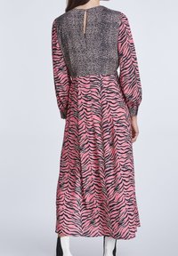Langes Kleid mit einem schwarz-pinken Tigerstreifen-Muster am unteren Teil und einem kontrastierenden Leopardenmuster an der Oberseite. Puffärmel und ein Rückenschlitz-Detail.