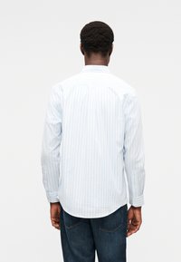 Ανοιχτό μπλε ριγέ πουκάμισο σε απαλό ύφασμα, με γιακά που κουμπώνει, μακριά μανίκια και καμπυλωτό τελείωμα. Φορεμένο με σκούρο τζιν.