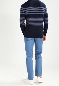 Pull bleu marine à rayures horizontales bleues, associé à un pantalon bleu clair et des baskets blanches, vu de dos. Tissu texturé.