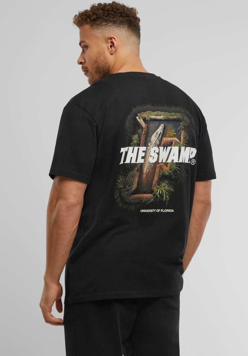 Sort bomuld t-shirt med et grafisk print af en alligator i en sumpe med teksten "THE SWAMP" og "UNIVERSITY OF FLORIDA" nedenfor.