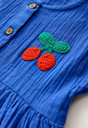 Niebieski teksturowany strój z motywem szydełkowym przedstawiającym dwa pomarańczowe owoce i zielone liście, ozdobiony drewnianymi guzikami z przodu.