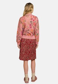 Embroidered pink bomber jacket with floral patterns, paired with a red floral skirt. Features ribbed cuffs and hem, and soft texture.