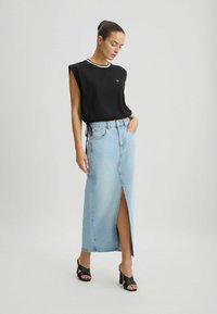 Zwarte mouwloze top met een witte halslijn, gecombineerd met een lichtblauwe denim maxi rok met een split aan de voorkant en een relaxte pasvorm. Zwarte hakken.