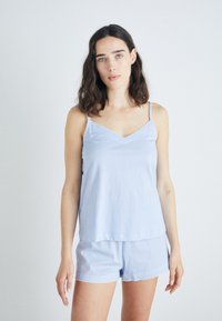 Svetlo modra pyžama iz trakov s camisole vrhom z V-izrezom in kratkimi hlačami. Tkanina je mehka, z valovitimi robovi ob robu in trakovih.