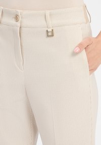 Beige karierte Hose aus strukturiertem Stoff, mit einer Vordertasche, Knopfverschluss und quadratischer Hardware-Akzentuierung.