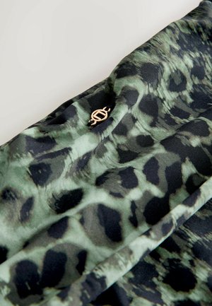 Grün-schwarz gemusteter Stoff mit glatter Textur, verziert mit einem goldenen Emblem. Das Design ähnelt einem Leopardenmuster.