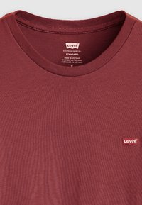 Red cotton t-shirt with a round neck, ribbed collar, and small Levi's logo tag in the bottom left corner. Textured surface.