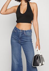 Czarny top na halter z niskim dekoltem, w połączeniu z niebieskimi jeansami o wysokim stanie. Modelka trzyma małą torebkę w czarno-białym kolorze.