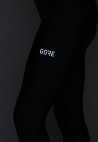 Svarta träningstights i stretchmaterial, med en vit "GORE"-logotyp på låret. Slät yta med figursydd design och minimala sömmar.