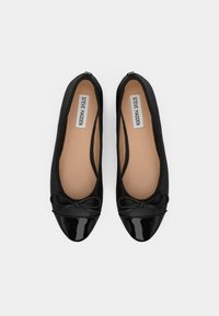 Mustat ballerinakengät pehmeästä materiaalista, patenttinahkainen kärki ja rusetti koristuksena. Sisäpuolella on neutraalin beige vuori.