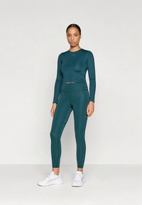 Türkizkék hosszú ujjú crop top és magas derekú leggings rugalmas anyagból, kis logó díszítéssel és sima textúrával.