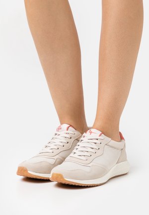 Baskets beiges en matières mesh et daim, avec une semelle blanche rembourrée et des accents corail au niveau du talon et de la languette, lacets détaillés.