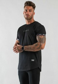 Svart t-shirt med kort ärm och rund hals, med vit "LIMIT"-tryck och mönstrade detaljer på ärmarna.