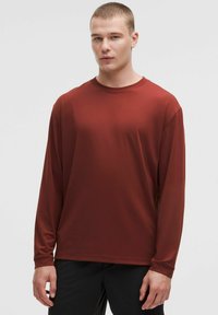 Långärmad, rostfärgad träningsskjorta gjord av mjukt, elastiskt tyg. Har rund halsringning och avslappnad passform.