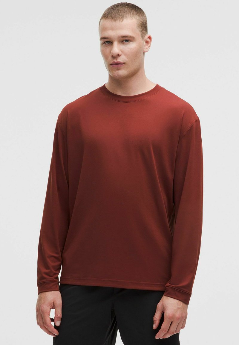 Långärmad, rostfärgad träningsskjorta gjord av mjukt, elastiskt tyg. Har rund halsringning och avslappnad passform.