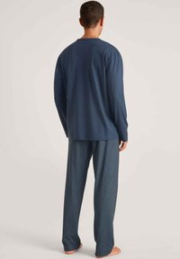 Marineblauwe long-sleeve shirt gecombineerd met gestreepte broek; het shirt heeft een ronde hals, terwijl de broek een geometrisch ontwerp in lichte kleuren toont.