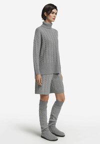 Jasnoszary dzianinowy sweter z wysokim kołnierzem, połączony z pasującymi szortami i skarpetkami do kolan, zdobiony fakturą warkocza.